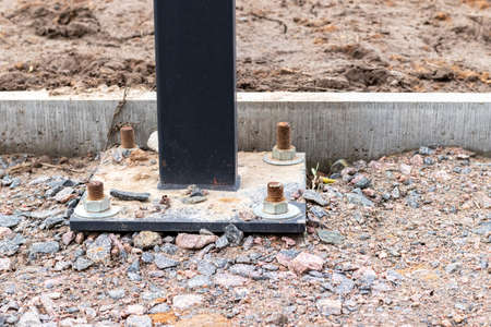Installation of a lighting column or billboard with four anchor bolts on a track of a construction site covered with gravel near a concrete curbの写真素材