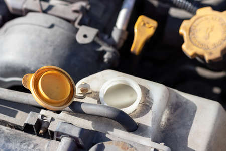 Open lid on an antifreeze tank. Dusty details of a flat-four (boxer) car engine compartment under the open hood. Closeup view on a sunny dayの写真素材
