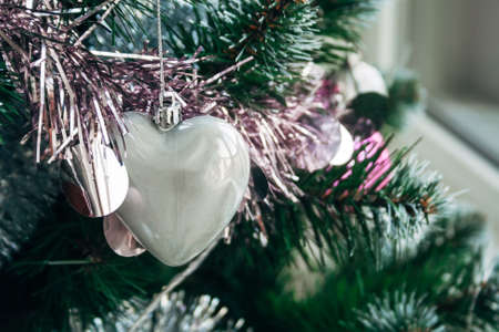 Silver white glossy heart and pale pink garland on artificial Christmas tree. Selective focus. Holiday card with decorations for the New Year's Eveの写真素材
