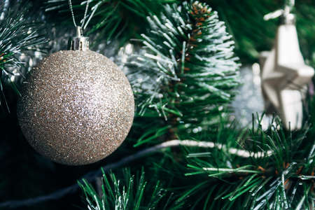 Beautiful golden sparkling ball on artificial Christmas tree. Selective focus. Holiday card with decorations for the New Year's Eveの写真素材