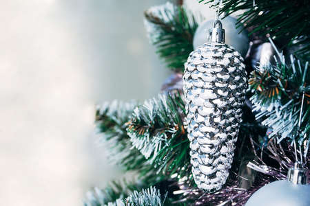 Silver white toy cone hanging on artificial Christmas tree with copy space. Selective focus. Holiday card with decorations for the New Year's Eveの写真素材