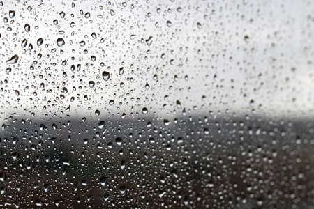 Drops of water on the glass against a blurred dark light gradient background on a rainy cloudy day. Selective focusの写真素材