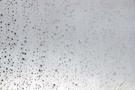 Raindrops on a window glass in rainy cloudy day against a gray sky. Autumn, depressive, rainy weather. Selective focusの写真素材