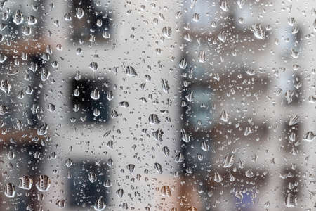 Drops of water on the window glass against a blurred background of a house on a rainy cloudy day....