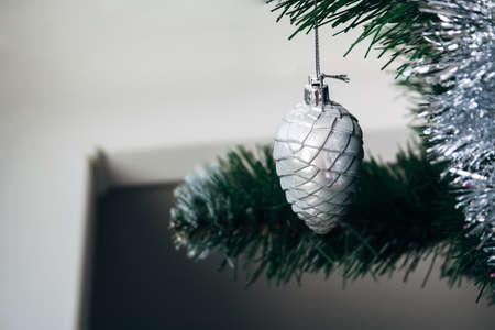 Silver white toy cone hanging on artificial Christmas tree with copy space. Selective focus. Holiday card with decorations for the New Year's Eveの写真素材