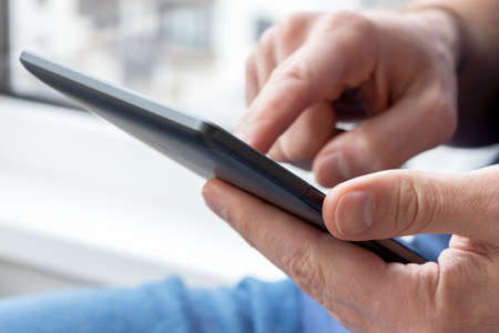 Gray e-reader electronic book in male hands. A man in with a tablet against a blurred background....