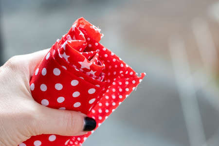 Female hand holds a roll of red and white fabrics against a blurred background. Selective focus. Closeup viewの写真素材