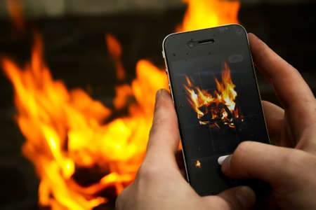 Men's hands take pictures of a bonfire on a mobile phoneの写真素材