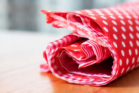 Roll of red and white natural cotton fabric on a wooden table. Selective focus. Closeup view. Blurred backgroundの写真素材