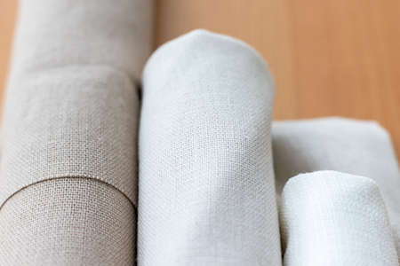 Three rolls of natural linen fabric in different colors on a wooden table. Selective focus. Closeup view. Blurred backgroundの写真素材