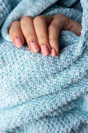 Female hand in blue knitted sweater fabric with trendy beautiful manicure - pink nude nails with...