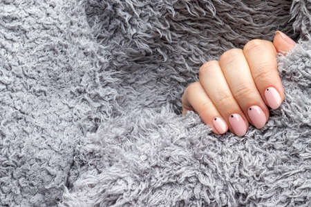 Female hand in a gray fluffy knitted sweater fabric with trendy beautiful manicure - pink nude nails with black small dots with copy space. Selective focus. Closeup viewの写真素材