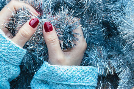 Female hands in a blue knitted sweater with a beautiful glossy manicure - burgundy, dark red, cherry...