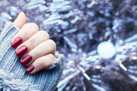 Female hand in a gray knitted sweater with a beautiful glossy manicure - burgundy, dark red, cherry...