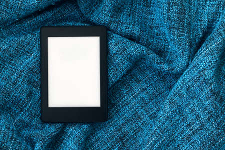 A modern black electronic book with a blank screen on a bright blue knitted blanket. Mockup tablet....