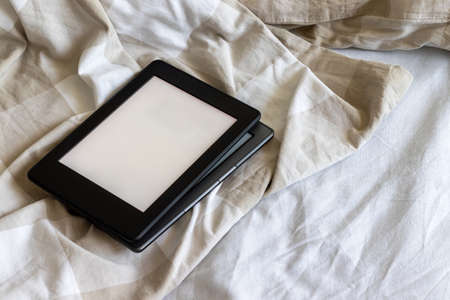 Two modern electronic books with a blank empty screens on a white and beige bed. Mockup tablets one...