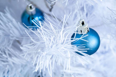 Closeup view of a blue matte ball hanging on a silver thread on a white artificial Christmas tree for a family holiday. Selective focusの写真素材