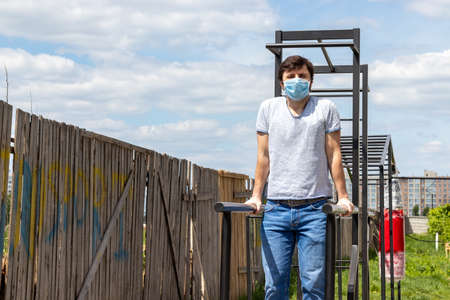Man in protective blue medical mask doing a bar stand on the outdoor sports ground with copy space....