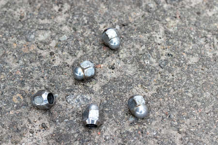 Five wheel nuts securing the wheel to the hub lie on the pavement near the car tire shop while...