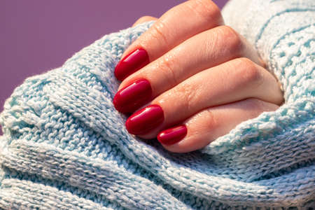 Female hand in a blue knitted sweater fabric with beautiful glossy manicure - burgundy, dark red color nails. Selective focus. Closeup viewの写真素材