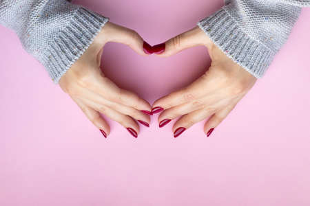 Woman's hands making heart symbol. Female hands in a gray knitted sweater fabric with beautiful...