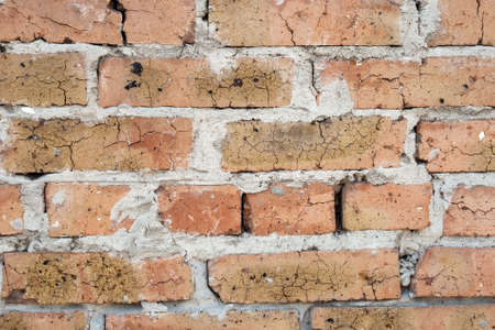 Wall of old orange red cracked brick with a thick layer of cement between them