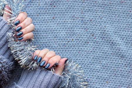 Female hands in gray knitted sweater with beautiful manicure - dark gray blue glittered nails on...