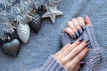 Female hands in gray knitted sweater with beautiful manicure - dark gray blue glittered nails on...