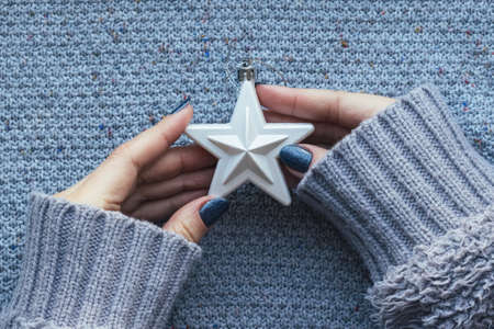 Female hands in knitted sweater with white Christmas tree star and with beautiful manicure - dark...