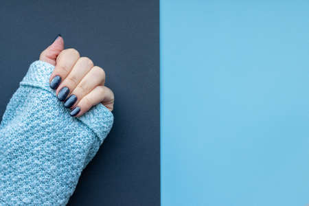 Female hand in knitted sweater fabric with beautiful manicure - dark glittered nails on gray and blue background with copy spaceの写真素材