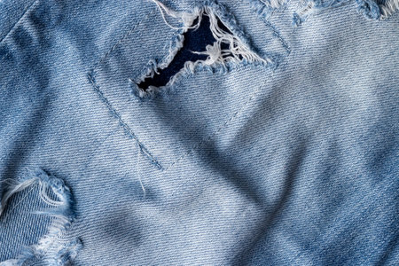 Blue torn jeans fabric texture. Distressed denim with hole and patch backgroundの写真素材