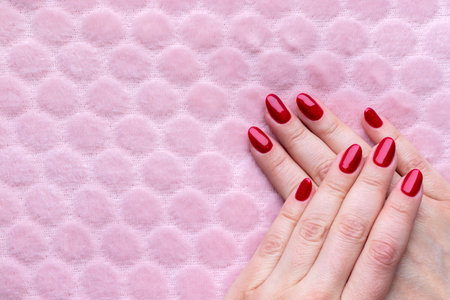 Female hands with beautiful manicure - red glittered nails on pink fluffy background with copy spaceの写真素材