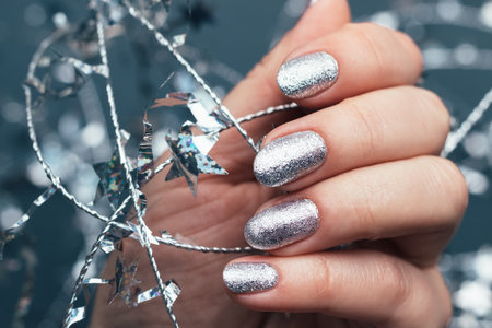 Female hand with beautiful holiday manicure - silver glittered nails with Christmas twisted wire with stars. Selective focus. Closeup view. Blurred gray backgroundの写真素材