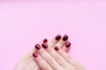 Female hands with beautiful manicure - dark red glittered nails on pink background with copy spaceの写真素材