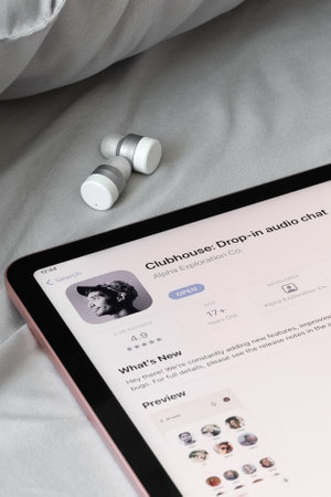 Clubhouse app drop in audio chat application in appstore on digital tablet and wireless bluetooth headphones on textile bedding. Vertical photo for social media. Kyiv, Ukraine - February 16, 2021のeditorial素材