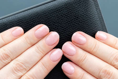 Female hands with beautiful manicure - pink nude nails on black leather surface on gray background. Closeup viewの写真素材