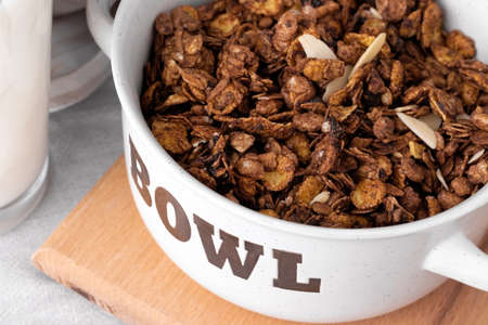 Organic homemade roasted granola cereal with oats, flax, almonds, chocolate in white round bowl with glass of milk on wooden tray or board on linen textile. Natural muesli breakfastの写真素材