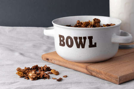 Organic homemade roasted granola cereal with oats, flax, almonds, chocolate in white round bowl with glass of milk on wooden tray or board on linen textile. Natural muesli breakfastの写真素材