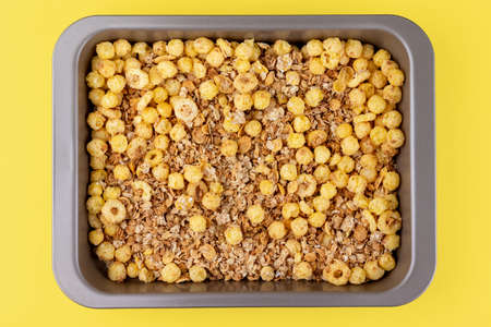 Organic homemade roasted crispy granola cereal with oatmeal and flaxseed flakes and crunchy corn balls and rings in baking tray on bright yellow background. Top view, flat lay muesliの写真素材