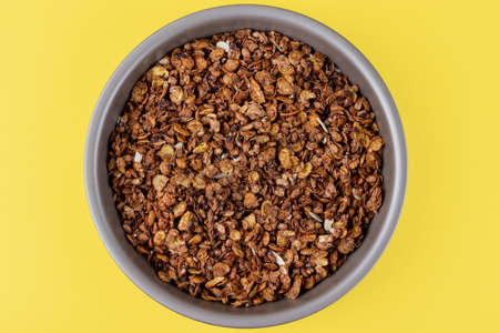 Organic homemade roasted granola cereal with oats, flax, almonds, chocolate in round baking tray on bright yellow background. Top view, flat lay muesliの写真素材