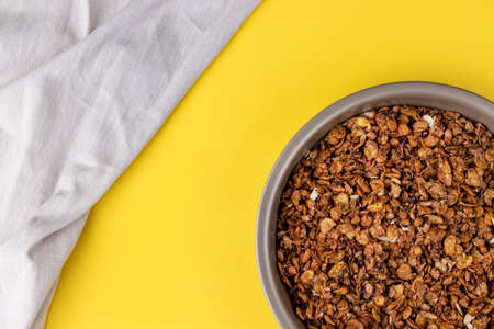 Organic homemade roasted granola cereal with oats, flax, almonds, chocolate in round baking tray with linen textile on bright yellow background. Top view, flat lay muesliの写真素材