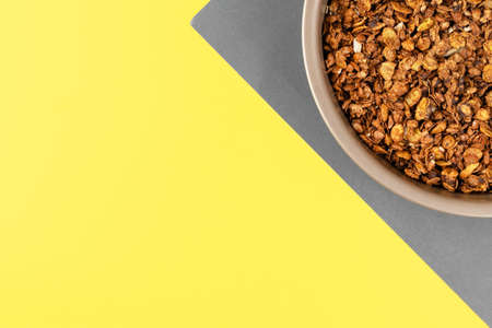 Organic homemade roasted granola cereal with oats, flax, almonds, chocolate in round baking tray on yellow and gray background. Top view, flat lay muesli with copy spaceの写真素材