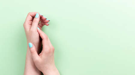 Female hands with beautiful manicure - mint blue nails on green background, banner with copy spaceの写真素材