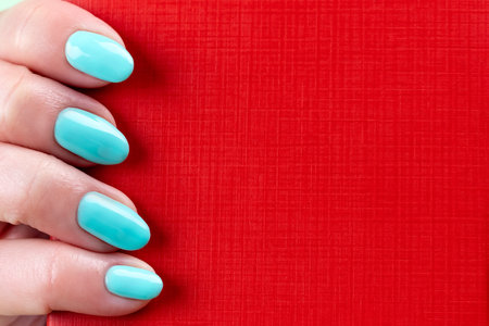 Female hand with beautiful manicure - mint blue nails with red leather surface, closeup with copy spaceの写真素材