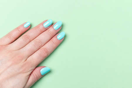 Female hand with beautiful manicure - mint blue nails on green background, closeup with copy spaceの写真素材