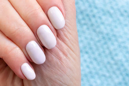 Female hands with beautiful manicure - white ivory nails on blue knitted sweater fabric background