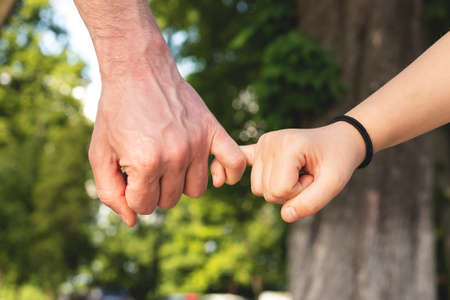 Father and child daughter hold on with their little fingers against blurred nature outdoor background. Trust, care and parenting family, father's day conceptの写真素材