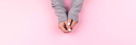 Female hands in gray knitted sweater with beautiful manicure - white nails on pink background, wide panoramic banner with copy space. Nail care conceptの写真素材