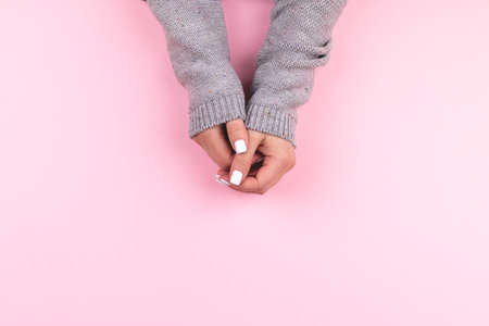 Female hands in gray knitted sweater with beautiful manicure - white nails on pink background, banner with copy space. Nail care conceptの写真素材
