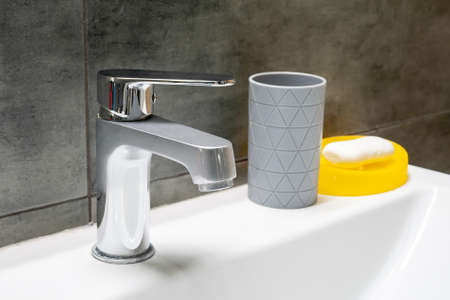 Misted chromed metal faucet for hot and cold water, gray cup for toothbrushes or cotton pads and a...